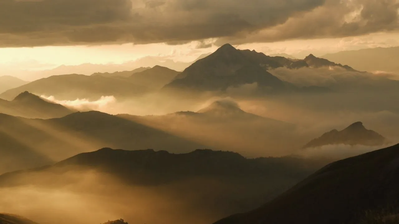 Montagne una dietro l'altra nella nebbia, attraversate da una luce dorata