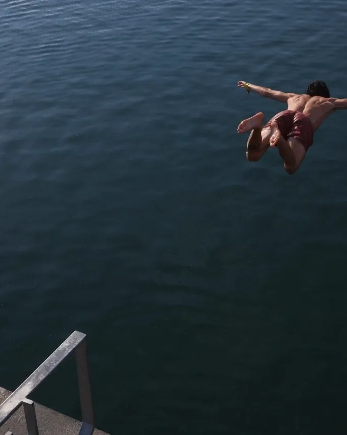 Un uomo si tuffa a braccia aperte dal pontile verso il mare scuro